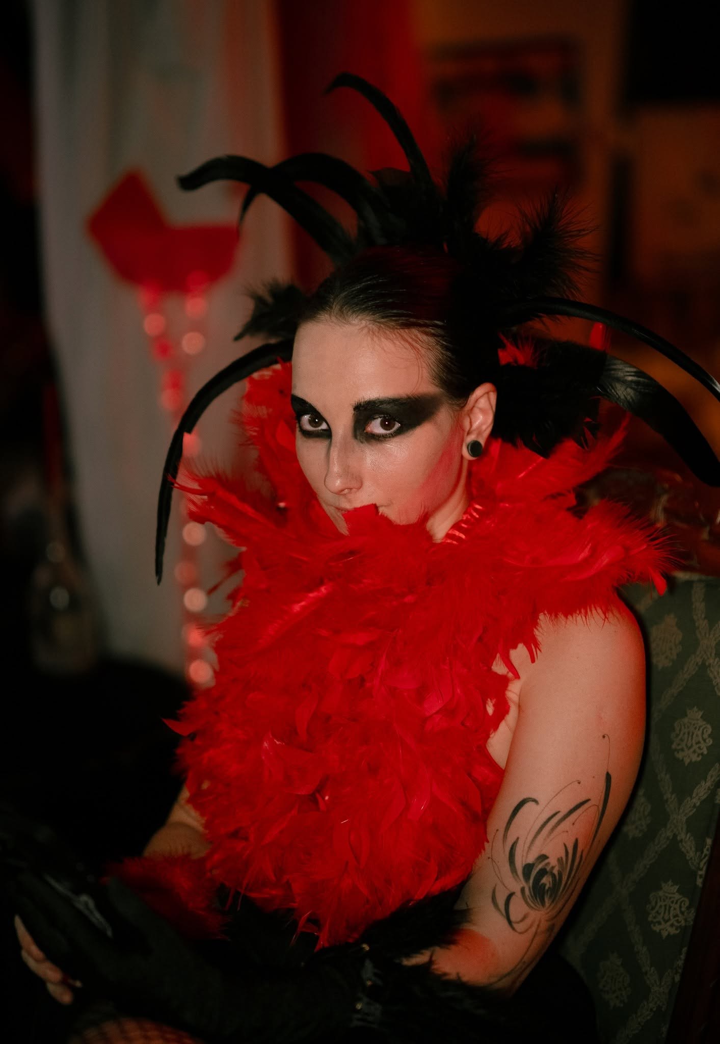 A guest with a black feather headpiece and a red feather collar