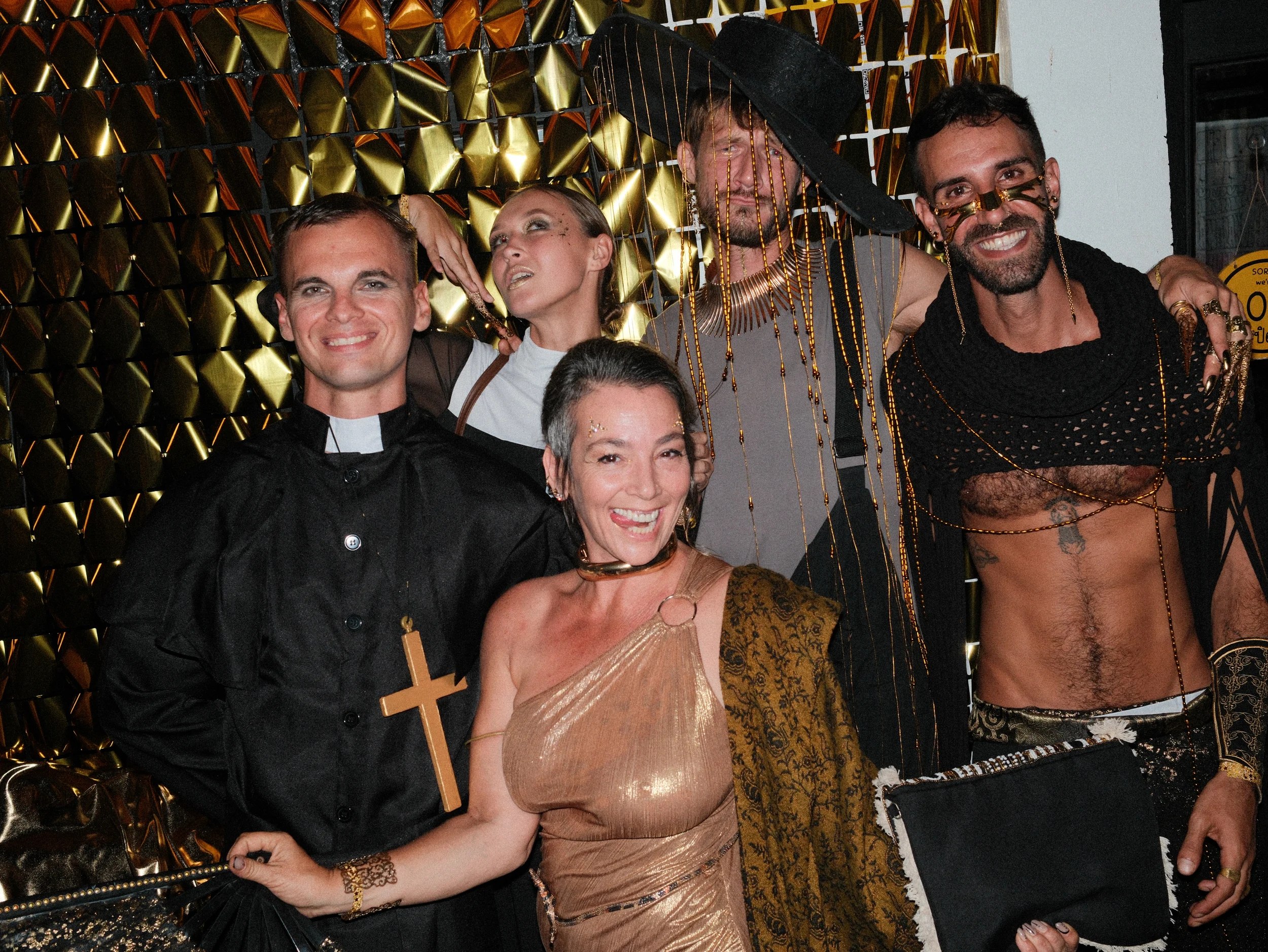 A group of guests in creative costumes against a gold backdrop