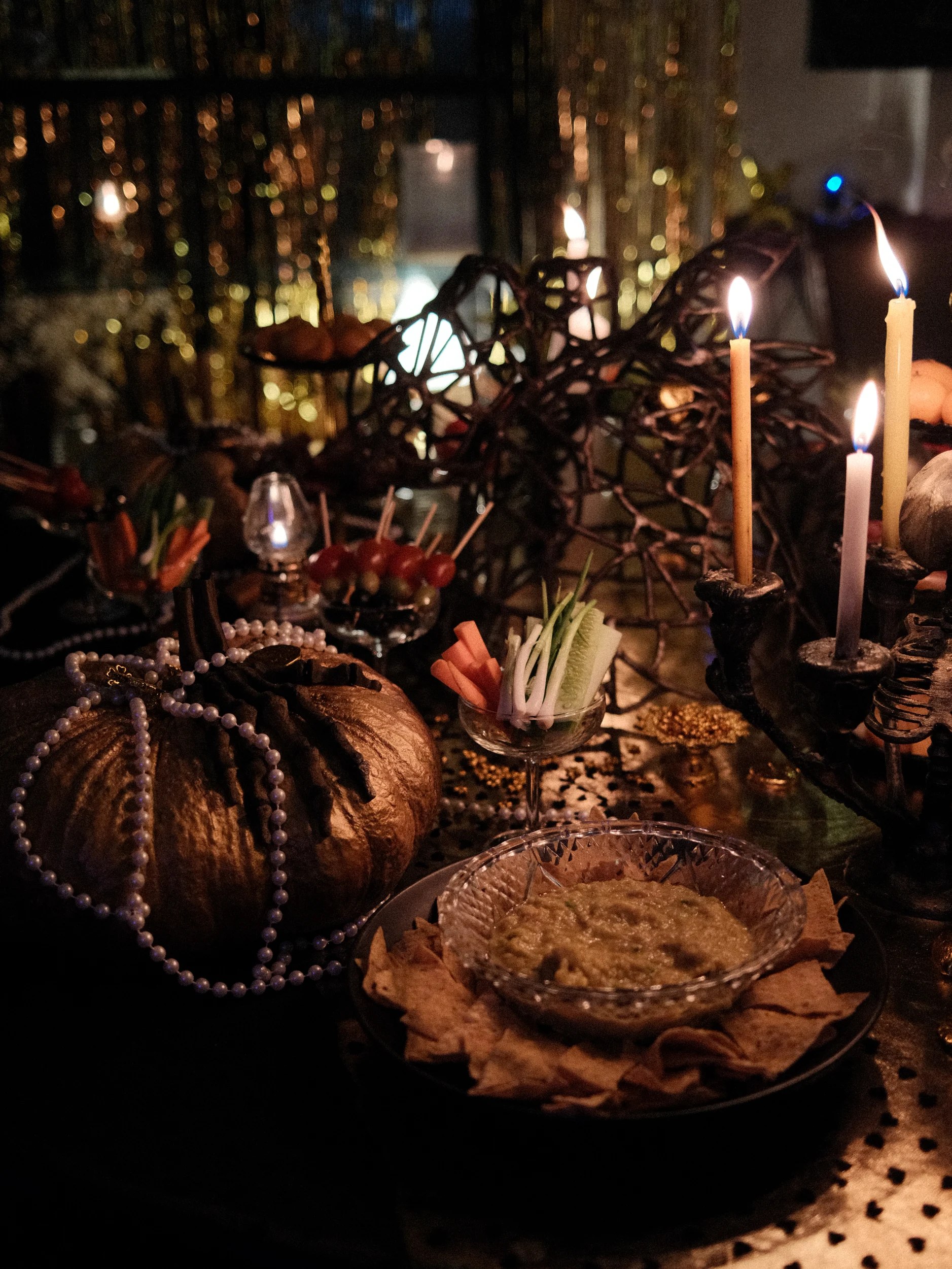 A candlelit buffet table with vegetables, a spread, pumpkins and gothic decorations